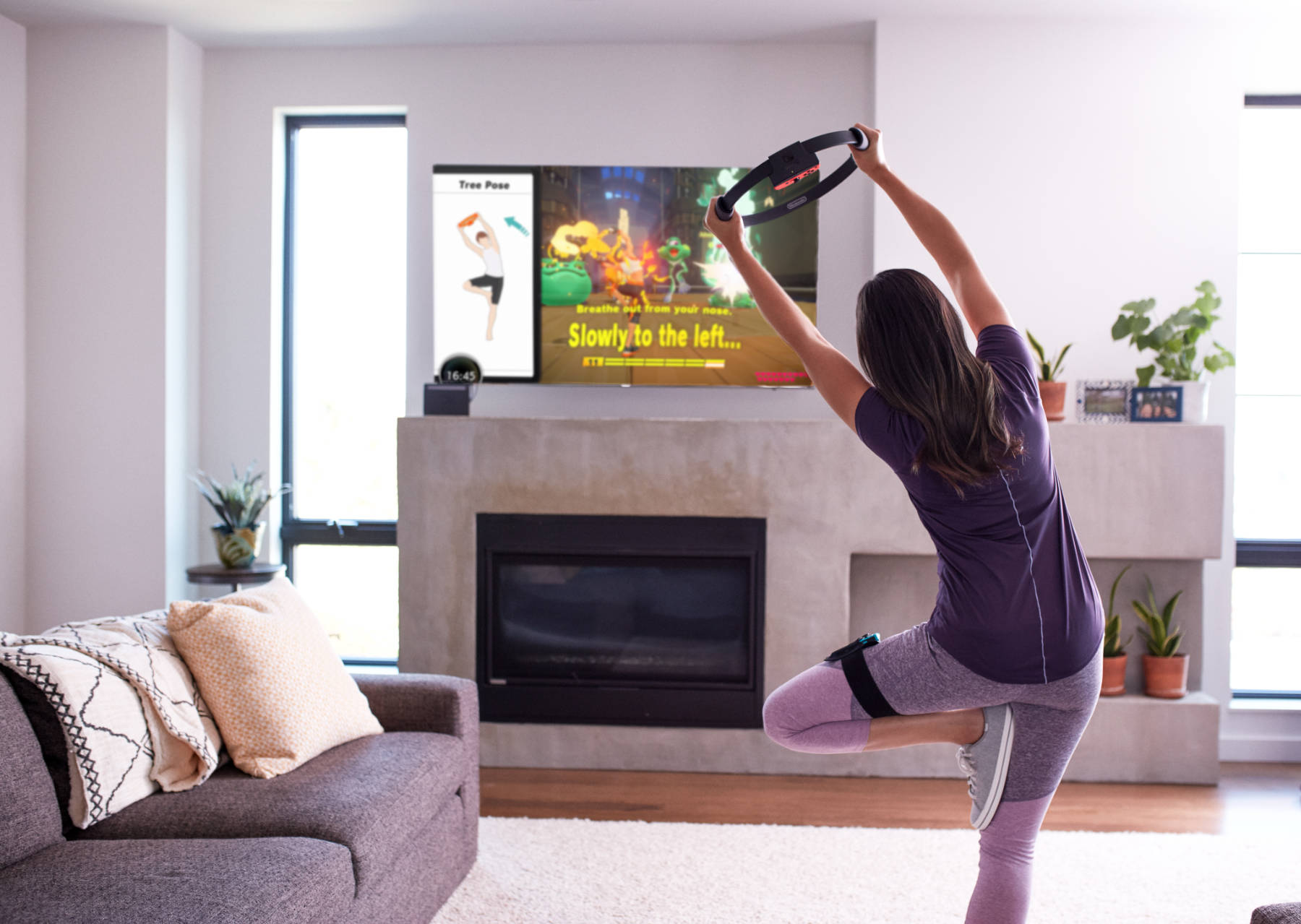 Woman in workout attire leans left in Tree pose with one Joy-Con in a strap on her left leg and the other in the Ring Con held above her head.