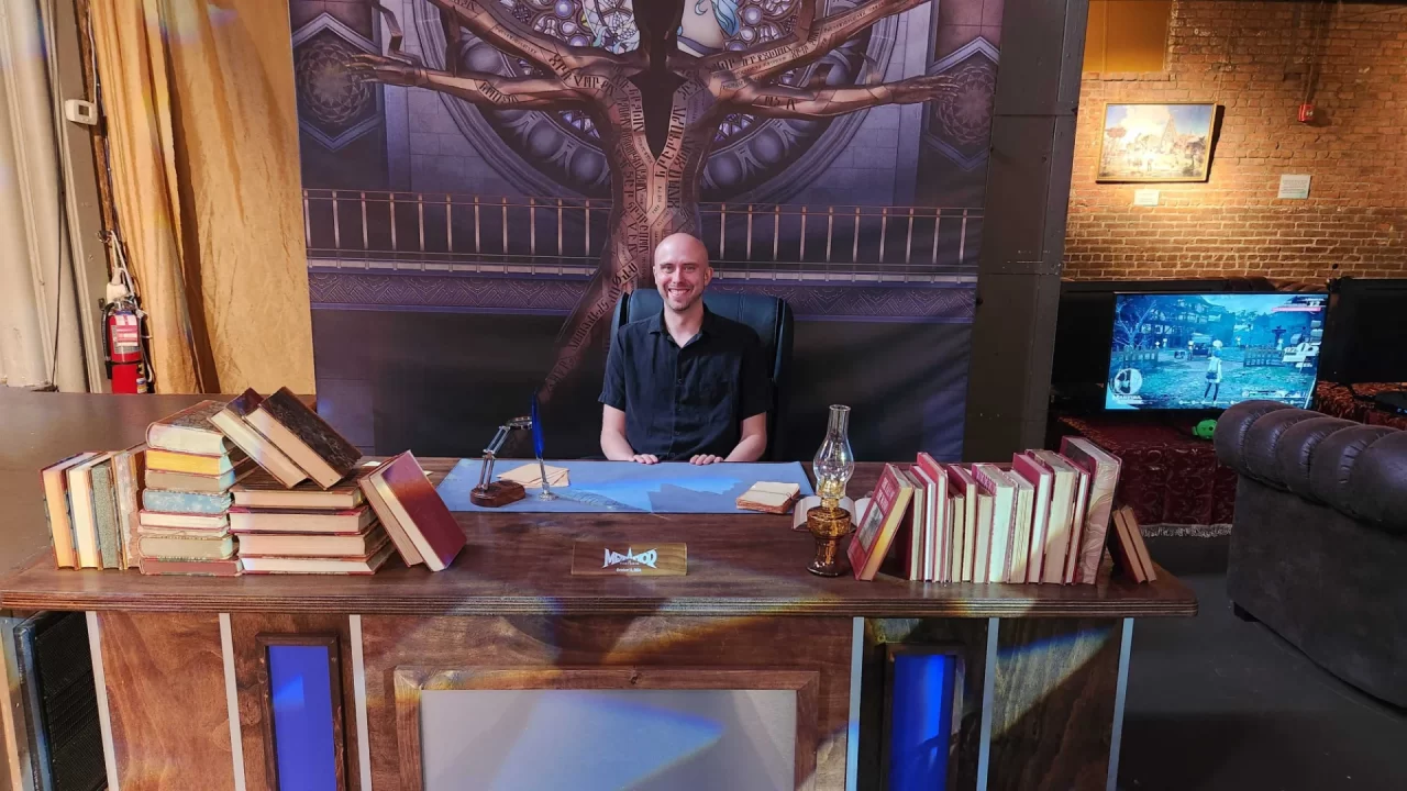 Metaphor ReFantazio Event Photo of Scott at a desk covered in books