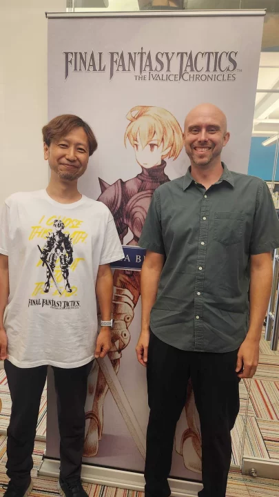 Scott Clay with Kazutoyo Maehiro in front a Final Fantasy Tactics The Ivalice Chronicles banner of Ramza
