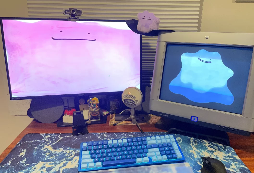 A picture of the author's computer desk, featuring screens of ditto and a ditto plush resting on a bridge made of hat insert between the two monitors.