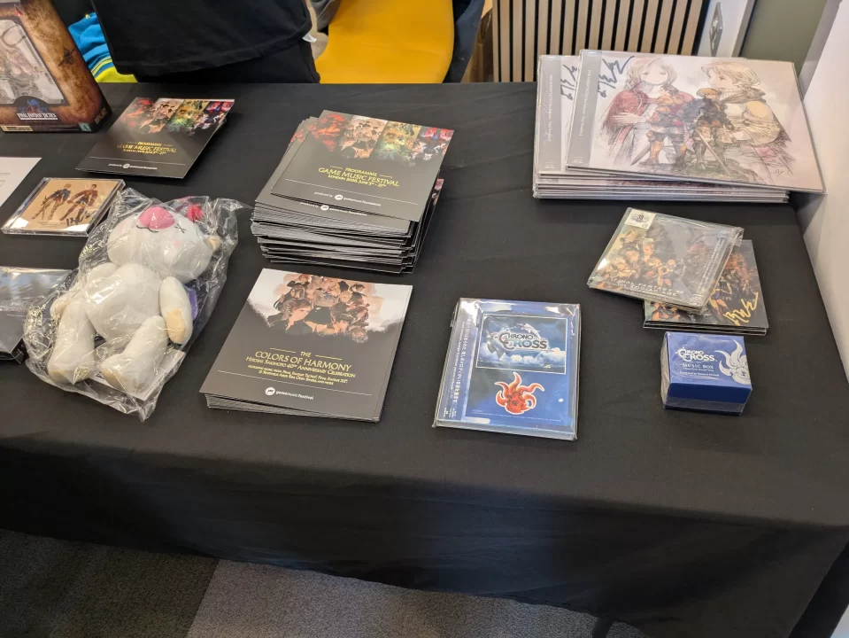 A merch table with music, programs, and a plush moogle.